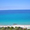 Spiaggia con sabbia bianca e mare azzurro, vegetazione sullo sfondo.