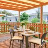 Un patio in legno con tavolo apparecchiato e sedie, circondato da vegetazione.
