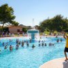 Persone in piscina seguono una lezione di acquagym, cielo sereno.