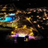 Veduta notturna di un villaggio turistico illuminato, con piscina e anfiteatro.