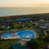 Complesso di piscine circondato da verde e vista sul mare al tramonto.