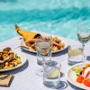 Piatti di cibo con frutti di mare e caprese, bicchieri di vino e acqua, davanti a una piscina.