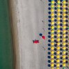 Ombrelloni gialli allineati su una spiaggia sabbiosa vista dall'alto.