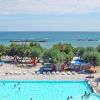 Una piscina vicino alla spiaggia, circondata da alberi e sdraio. Il mare si vede sullo sfondo.