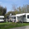 Camper parcheggiati su prato verde con persone sedute fuori a rilassarsi.