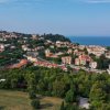 Vista aerea di una città costiera con colline verdi e il mare sullo sfondo.