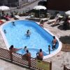 Piscina all'aperto con persone che nuotano e prendono il sole sotto ombrelloni bianchi.