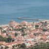 Vista di una città costiera con edifici dai tetti rossi e un molo sul mare.