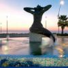 Fontana con una statua artistica al tramonto, circondata da palme.